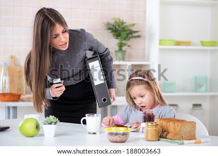 Overworked Mother Rushing her little daughter in the morning to go faster because she late for work. Daughter having breakfast. Mother and Daughter getting angry with each other because of stress.