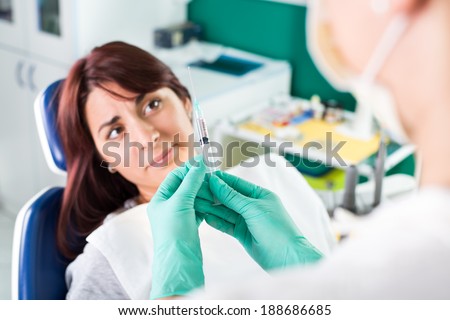 Young female dentist giving anesthesia to the patient before dental surgery. The patient in fear Expressing Negativity. Selective focus, focus on the patient.