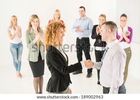 Two successful business people shaking hands at the meeting. Group their colleague celebrating in the background.