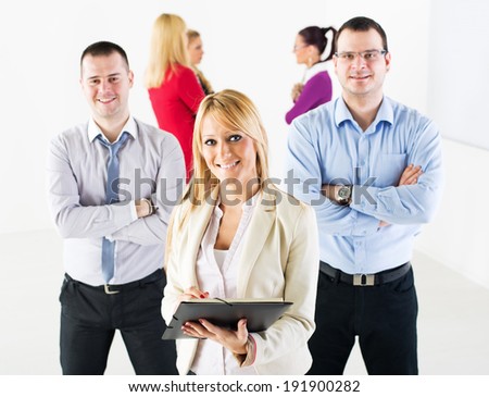 Three smiling co-workers standing in the office in front of their colleague. They are looking at camera.