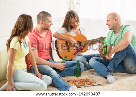 Four friends enjoying with guitar and beer together at the home party.