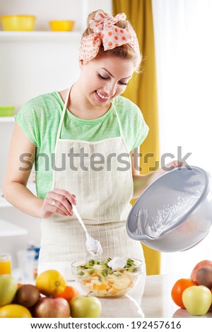 Beautiful young woman preparing fruit salad with Whipped Cream in the kitchen.