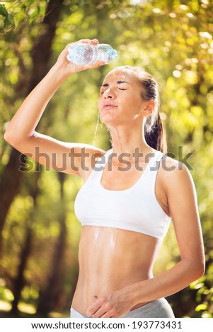 Young beautiful woman refreshing in the nature. She is refreshed with water from a bottle.