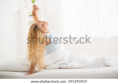 Cute young woman awakening in the morning. She is stretching in the bed.