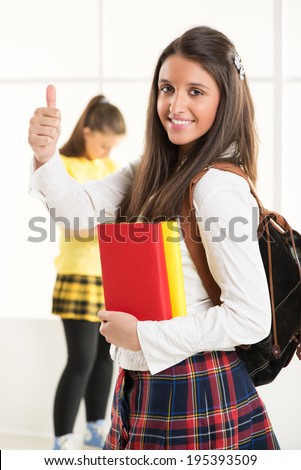 Happy beautiful teenage girl with Colorful books and school bag showing thumbs up