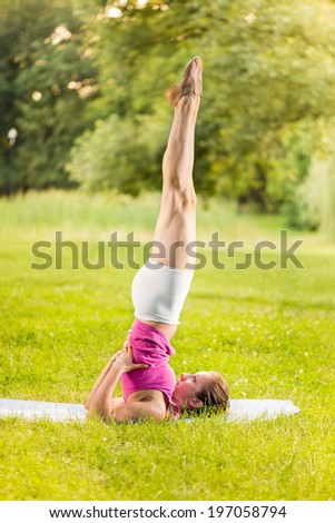 Young woman practicing yoga in the park. She is doing shoulder stand.