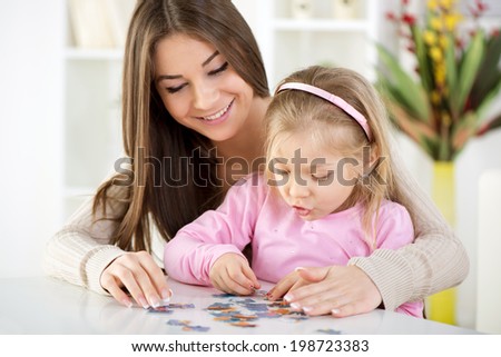 Mother and daughter playing at home. They assembling Jigsaw Puzzle.