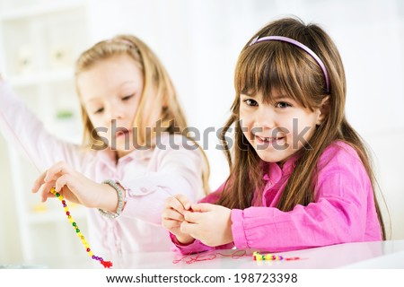 Two cute little girls Making bead jewelry at home