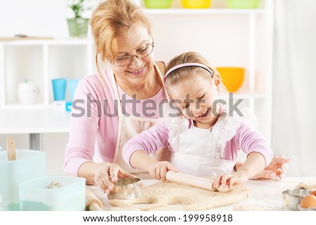 Beautiful happy grandmother and granddaughter a rolling pin together in the Kitchen.