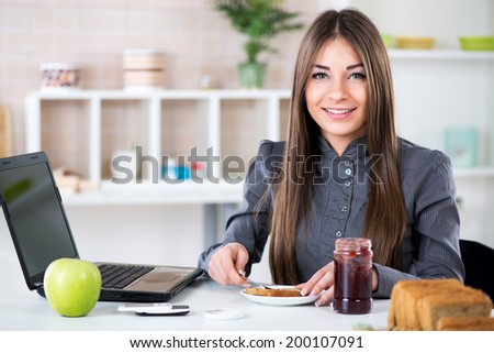 Businesswoman in the kitchen preparing breakfast. She is smearing jam on bread before going to work.
