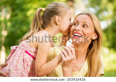 Cute little girl whispering with her mother in the park