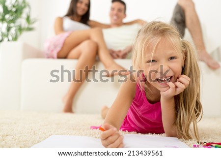 Happy family at home. Mother and father sitting, their cute little girls lying down and drawing with colored pencils. Focus On little girl.