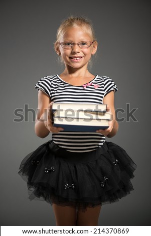 Cute little girl standing and holding books. Studio shutting. Grey background. Looking at camera.