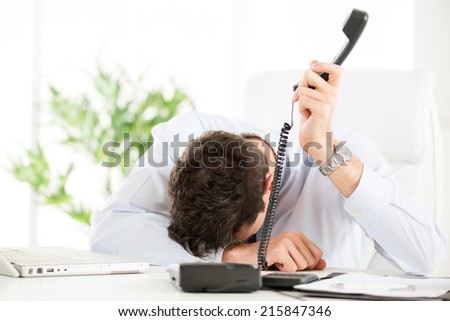 Tired young Businessman holding telephone and leaning his head on the table in the office.