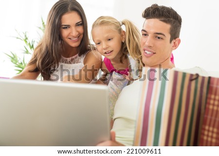 Beautiful happy family sitting at home with laptop and shopping bags.