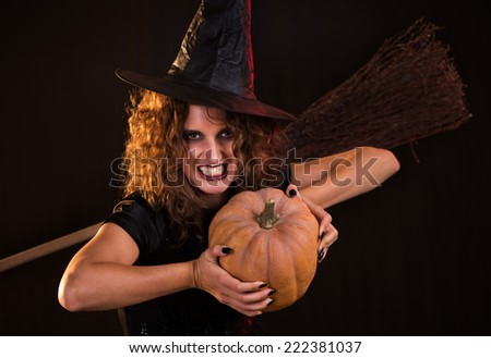 Young woman dressed like a witch. She is in dark clothing and holding a pumpkin.