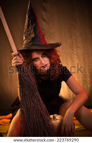Young woman dressed like a witch. She is in dark clothing with broom.
