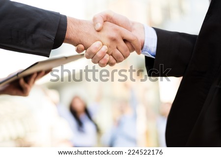 Hands of two business men shaking hands in the background can be seen by business people and office building.