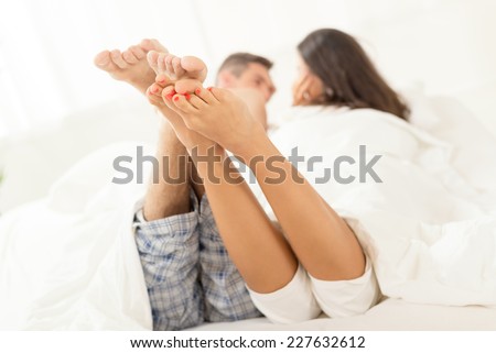 The legs of a young heterosexual couple relaxing in bed. Selective Focus, focus on the legs.