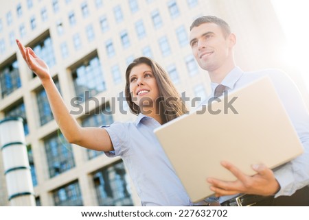 Young business couple with laptop, standing in front their company and look ahead at the height illuminated by the backlight of the sun\'s rays.