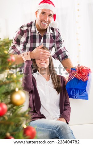 Young man gives his girlfriend a Christmas gift her hand over her eyes.