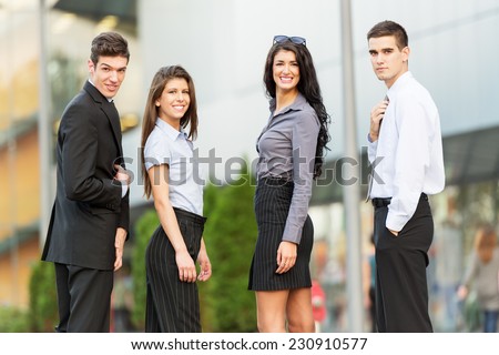 Portrait of group of young successful business people dressed in suits, standing in front of office building, smiling looking at camera.
