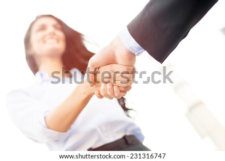 Business woman with face out of focus shakes hands with business man who can see only the hand.