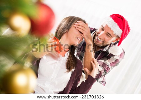 Young man gives his girlfriend a Christmas gift holding his hand over her eyes.