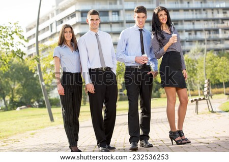 Group of young successful business people on the coffee break in a park near their company, whose office building seen in the background.