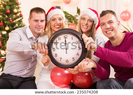 Happy friends Celebrating New Year in home interior and showing midnight on the clock. Selective Focus, focus on the clock.