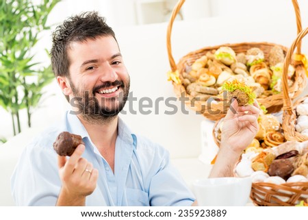 A young man with a beard, holding in his hands a sweet and savory pastries. With a smile looking at the camera. In the background you can see woven baskets with pastries.