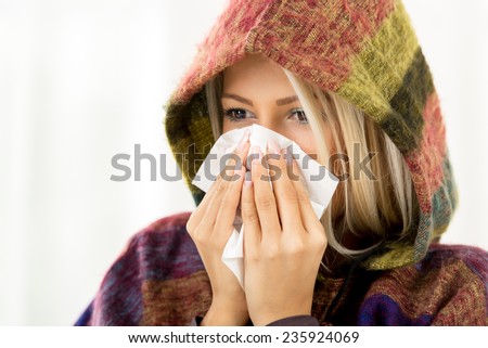 A beautiful girl with a hood on her head, holding a handkerchief to her nose.
