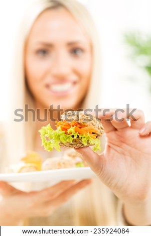 A young blonde woman with face out of focus keeps at arm\'s pastry offering the viewer snack.