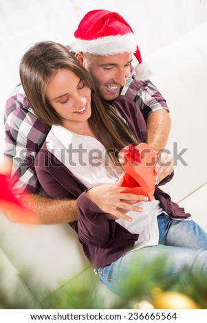 Young man gives his girlfriend a Christmas gift. She is happy while opening gift box.