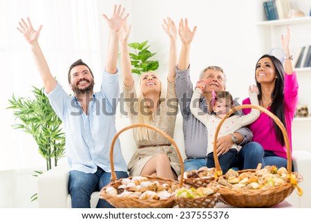 Happy family sitting on couch with arms raised, looking up. In front of them on the table are woven baskets decorated with beautiful pastries.