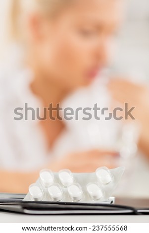 Close-up pills that stand on folder. In the background is out of focus blonde girl.