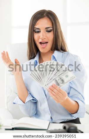 Young businesswoman holding money in hand and with an expression of surprise on her face looking into money.