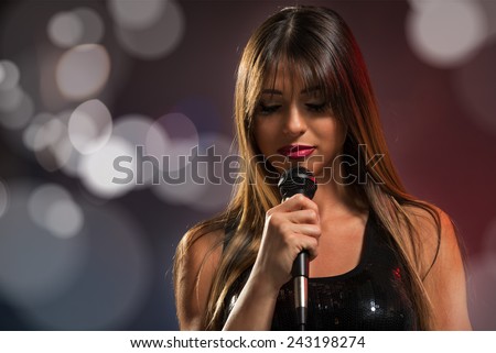 A young pretty woman singer, singing with eyes closed, holding a microphone.