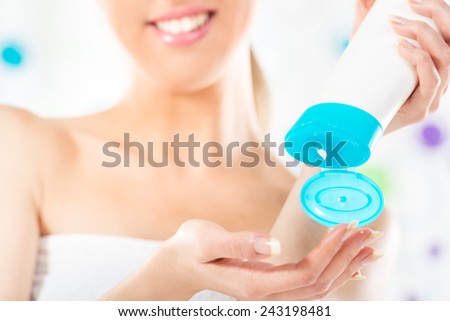 Close-up tube of cosmetic products in the hands of a young woman, unrecognizable face with a towel wrapped around her chest.