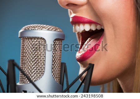 Close-up of female open mouth with red lipstick in front of microphone.