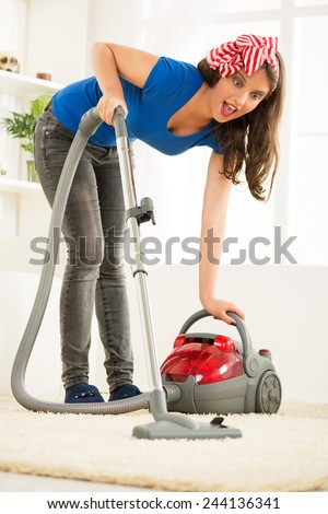 A young housewife vacuums the carpet in the room with an expression of surprise on her face.