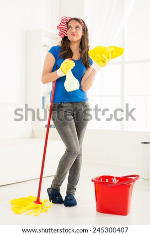 Young housewife with equipment for cleaning the house, standing in a room and think where to start cleaning up.
