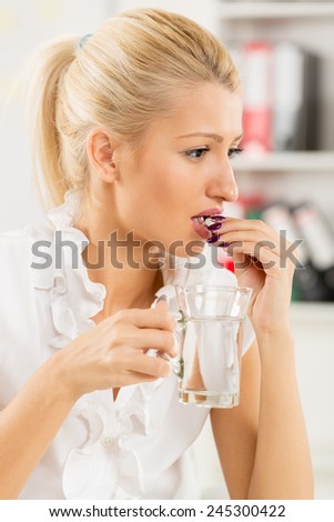 Young beautiful blonde woman takes a pill in the workplace, in the background you can see the shelves with binders.