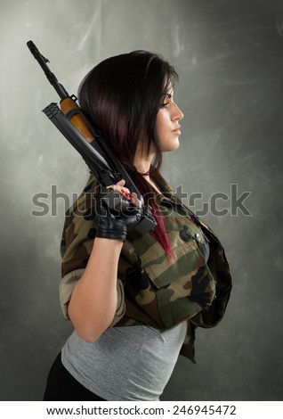 Profile of an attractive young women in military camouflage shirt with a Kalashnikov in her hand.