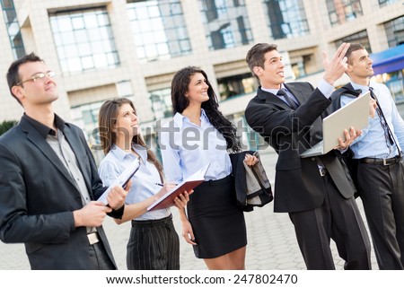 Young businessman with laptop in front of office building outstretched fingers of the hand, aimed at heights, explaining his colleagues business plan.
