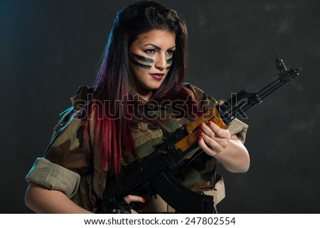 Attractive young woman with face paint on war paint in uniform holding an automatic rifle.