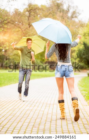 Meeting of young girl and a guy in the park, while holding umbrellas rushing into each other\'s arms.