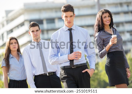 Young businessman, elegantly dressed, standing  with his team on a coffee break in front of office building and looking at the camera with a serious expression on his face.