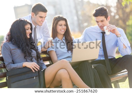 Small group of young business people sitting on a park bench during a break looking at the laptop.
