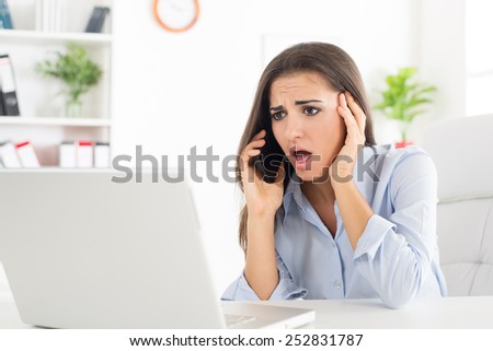 Young business woman, phoning at the office, with a worried expression on her face looking at laptop which is in front of her.
